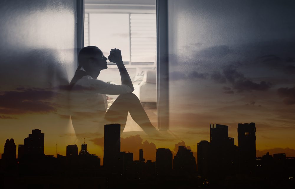 Silhouette of woman in prayer sitting in window with overlay of city sunset layered in front