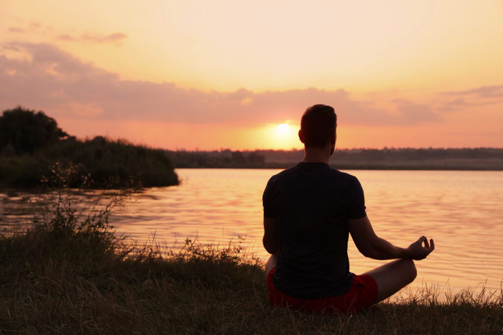Young man sitting near lake in meditation.