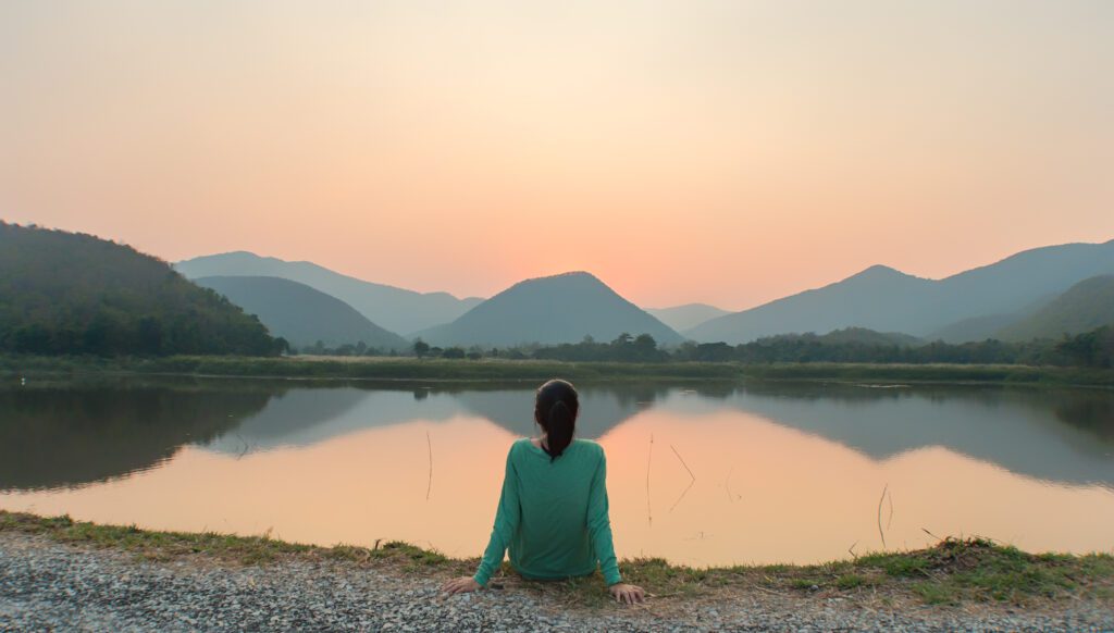 Woman sitting peacefully by lake and hills