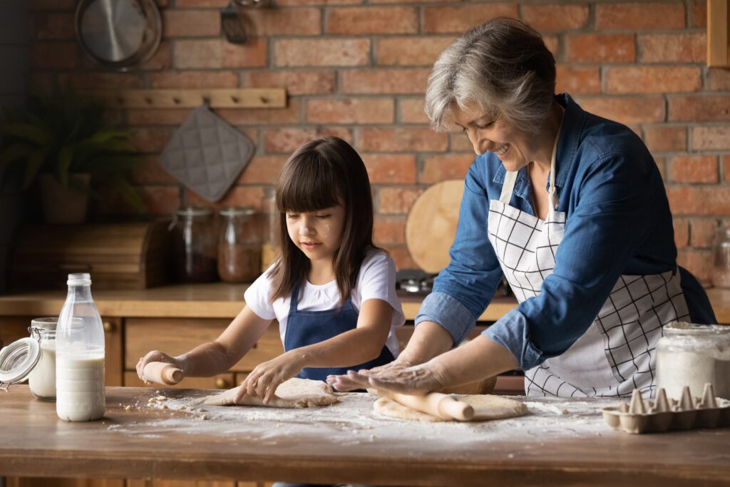 Grandmother and granddaughter rolling dough for baking